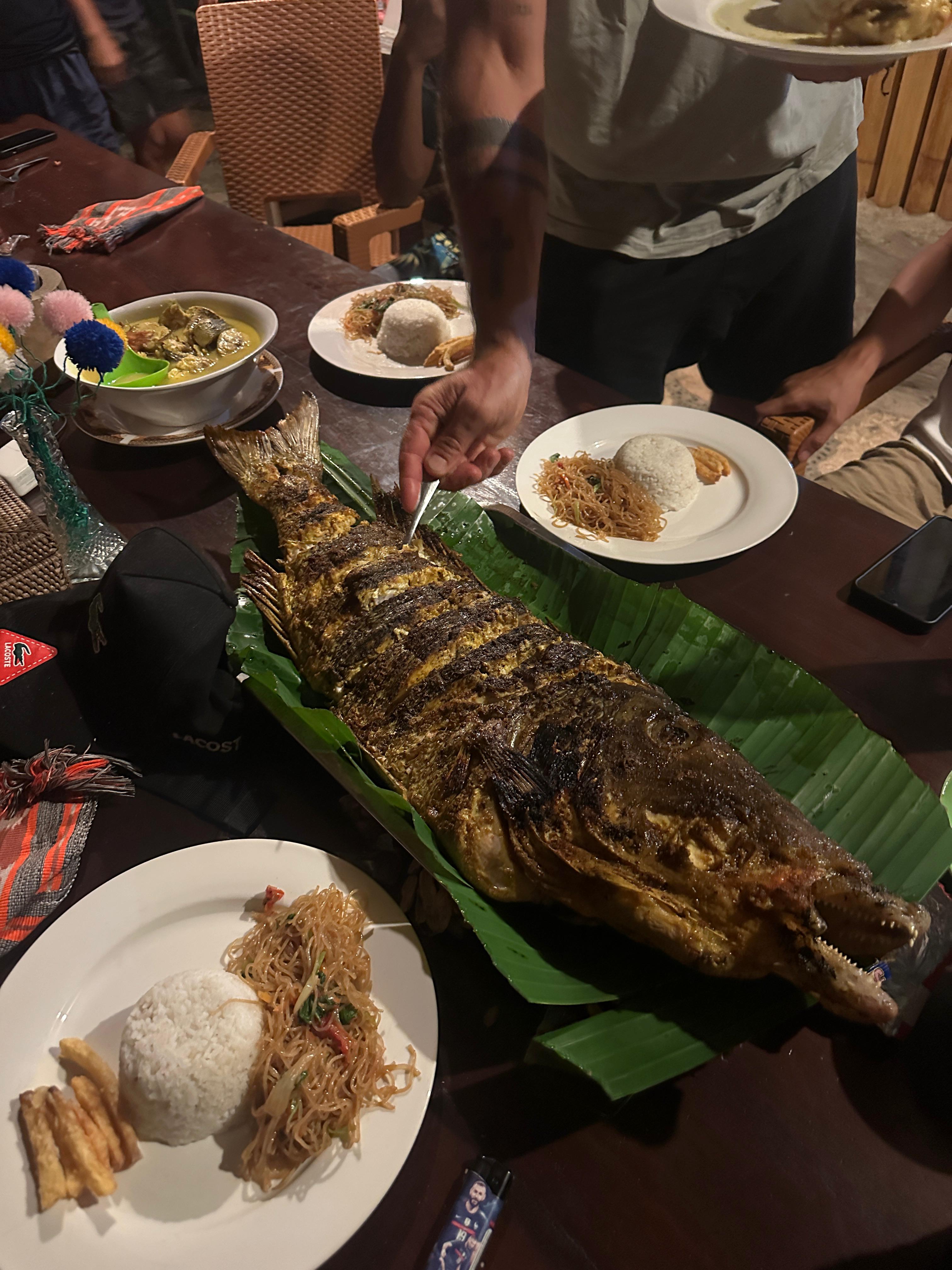 Shared BBQ dinner table on the beach with grilled fish and sides